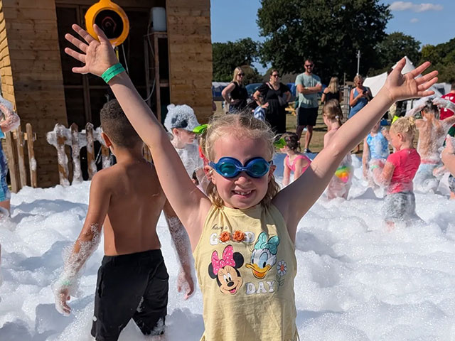 A young child wearing swimming goggles, enjoying a foam party at Wroxham Barns