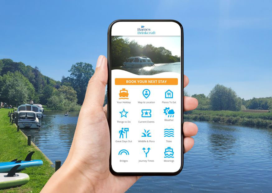 A hand holding a mobile phone, with a river view behind, the phone screen shows the Barnes Brinkcraft app home page